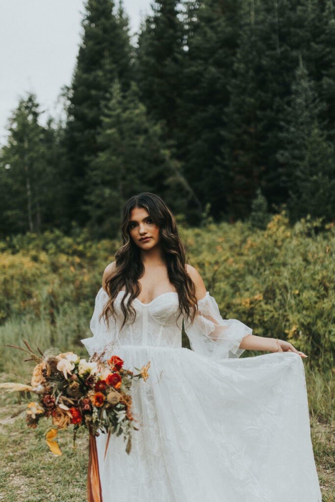 nature photo of a bride with her custom gown while holding a bouquet of flower