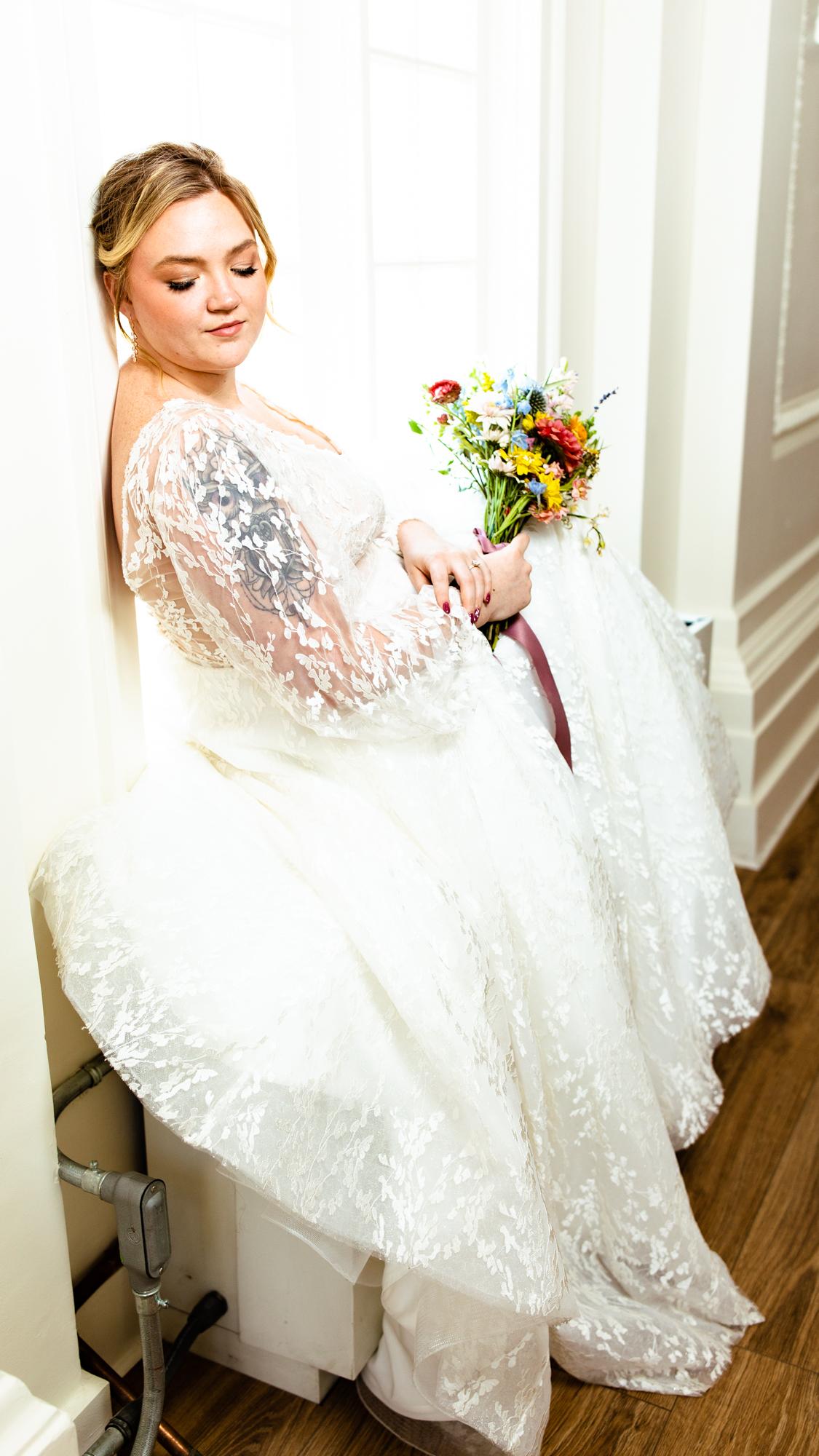 bride in her modest wedding dress sitting down while holding a bouquet