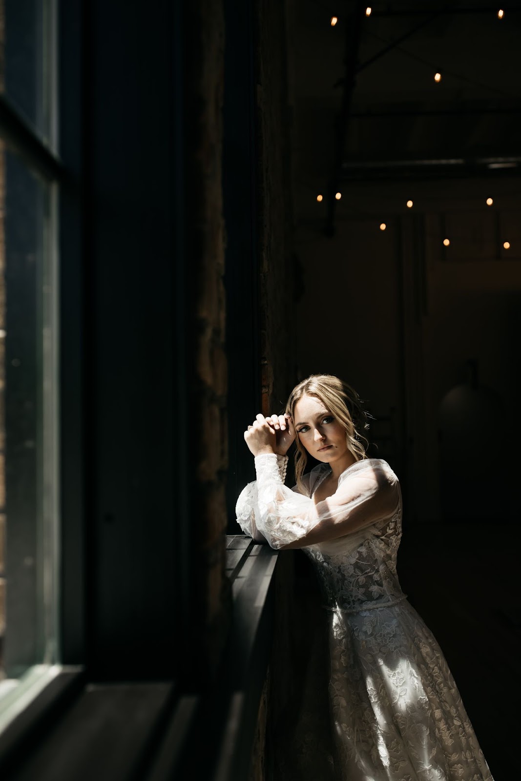 a bride in her long-sleeved, wedding dress posing by the window