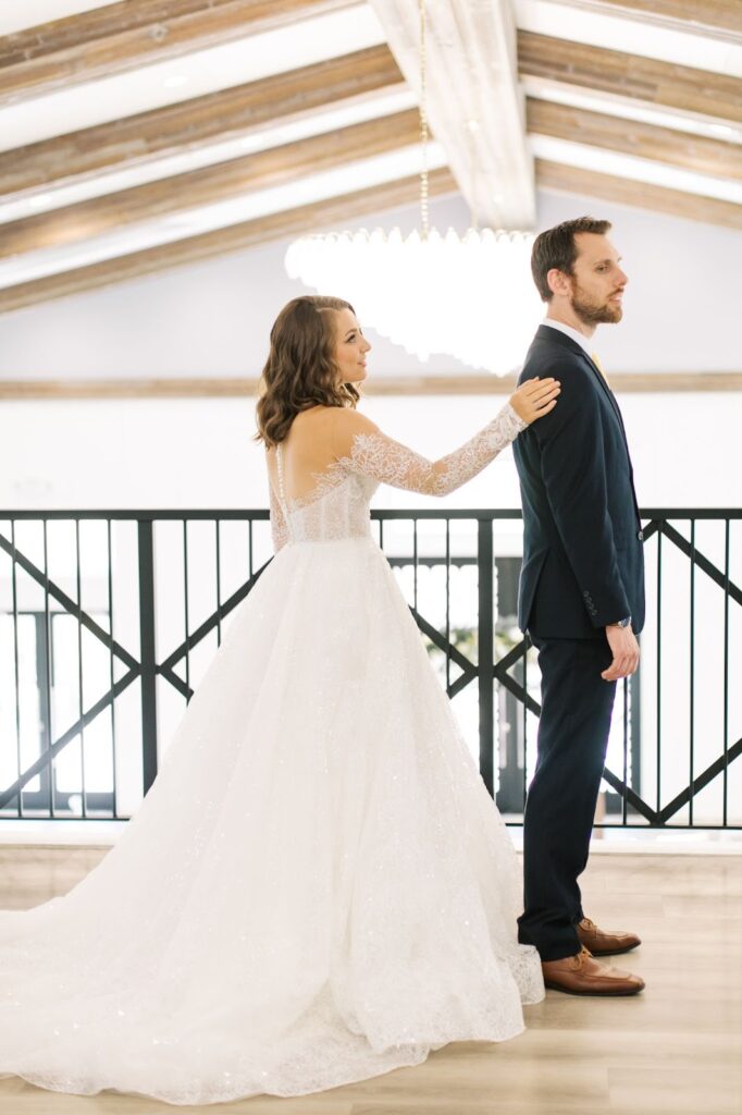 a bride in her ling-sleeved laced dress tapping his husband's shoulder