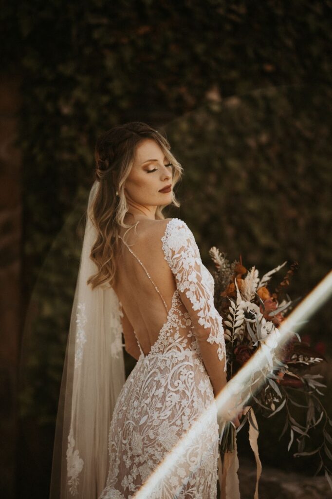a bride in her low back laced sleeves wedding dress while holding a bouquet