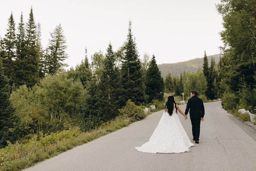 a bride and groom walking down the road while holding hands