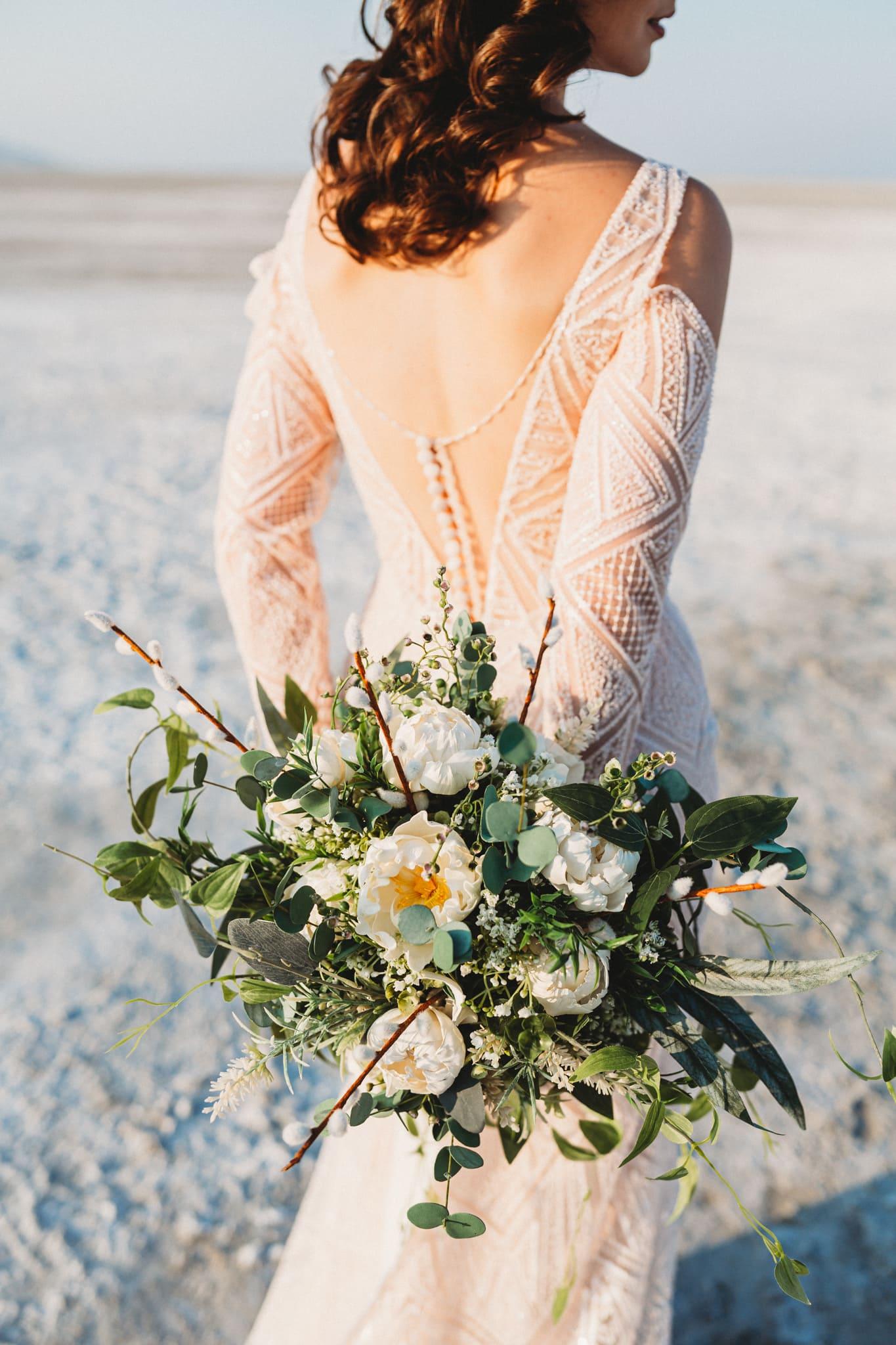 a back shot of a woman wearing a long sleeved wedding gown holding a bouquet of flower