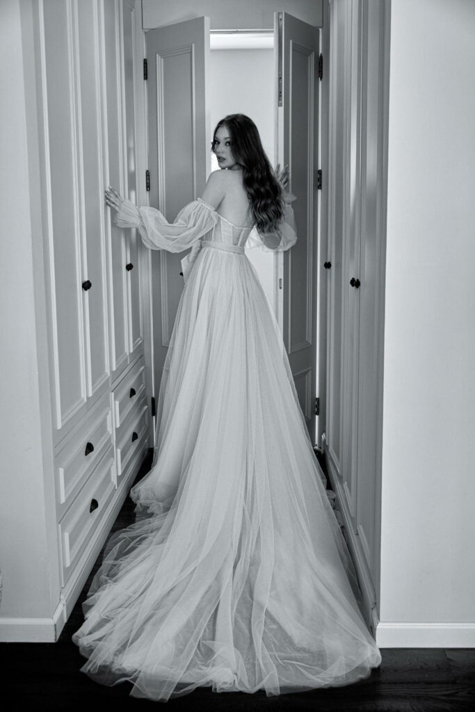 black and white image of a woman in wedding gown opening the door while looking back