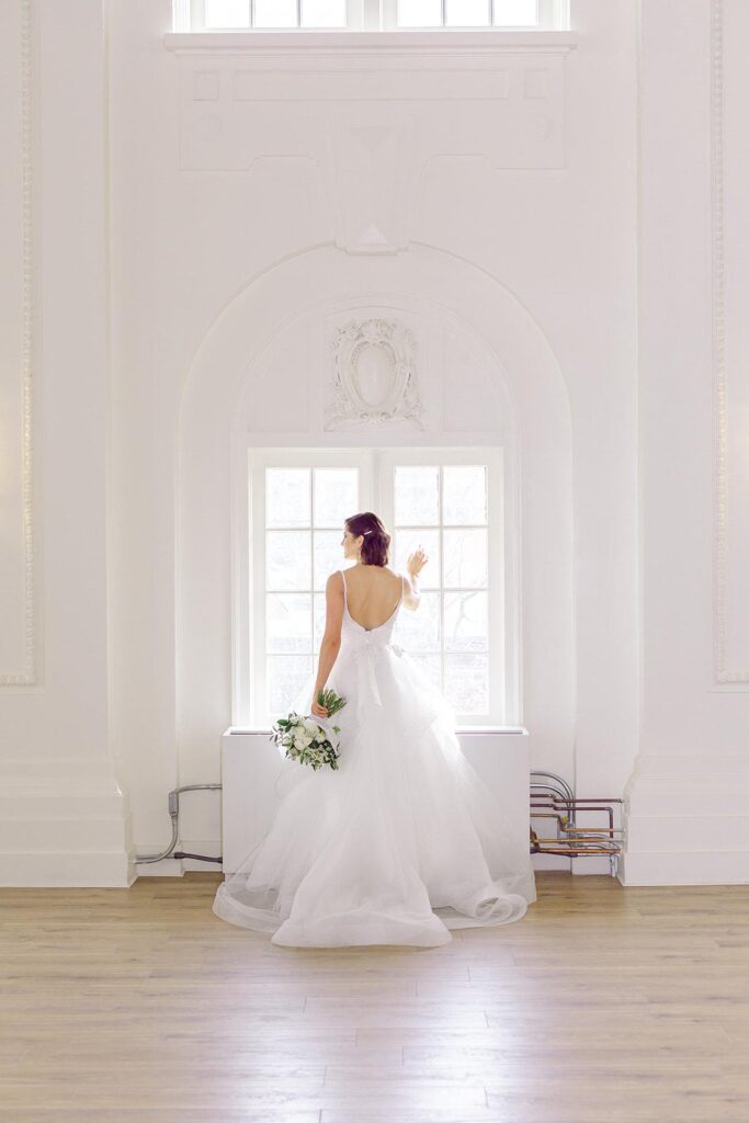 A bride in a white dress gazes out a window