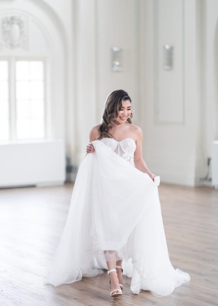 A bride wearing a white wedding dress stands in a spacious, empty room