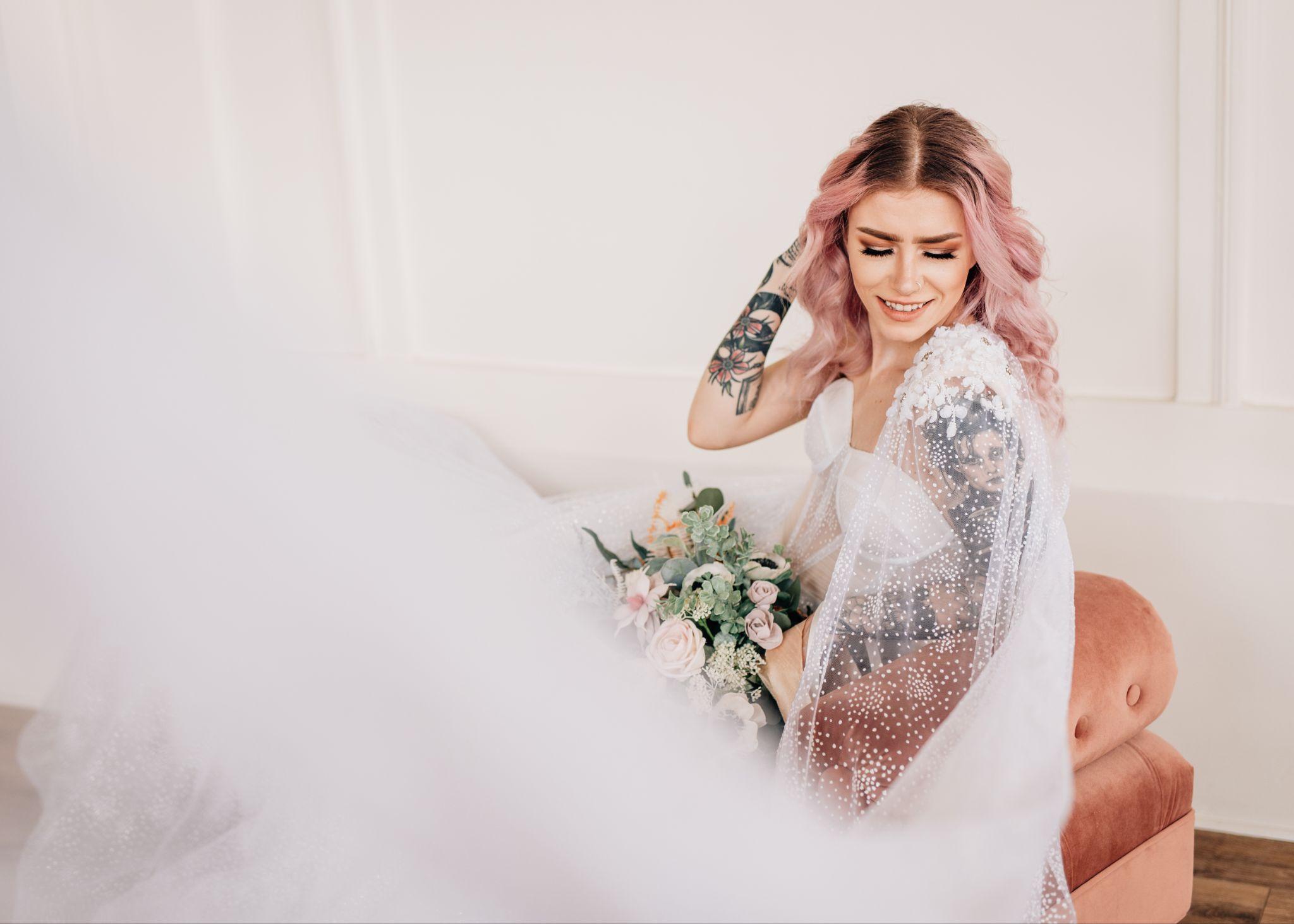 a bride with pink hair and tattoos lounges on a couch