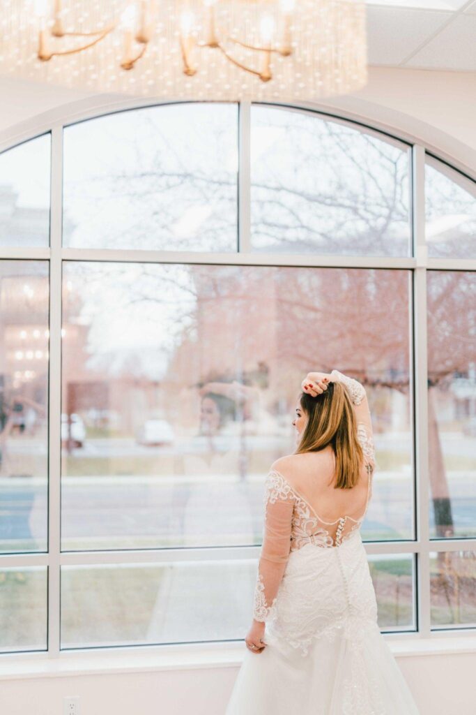 A woman wearing a white dress stands by a window
